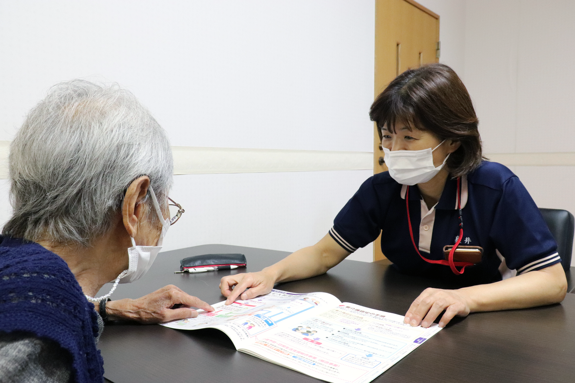 介護職員が高齢入居者に書類説明をしている様子。一対一の丁寧なケア場面。