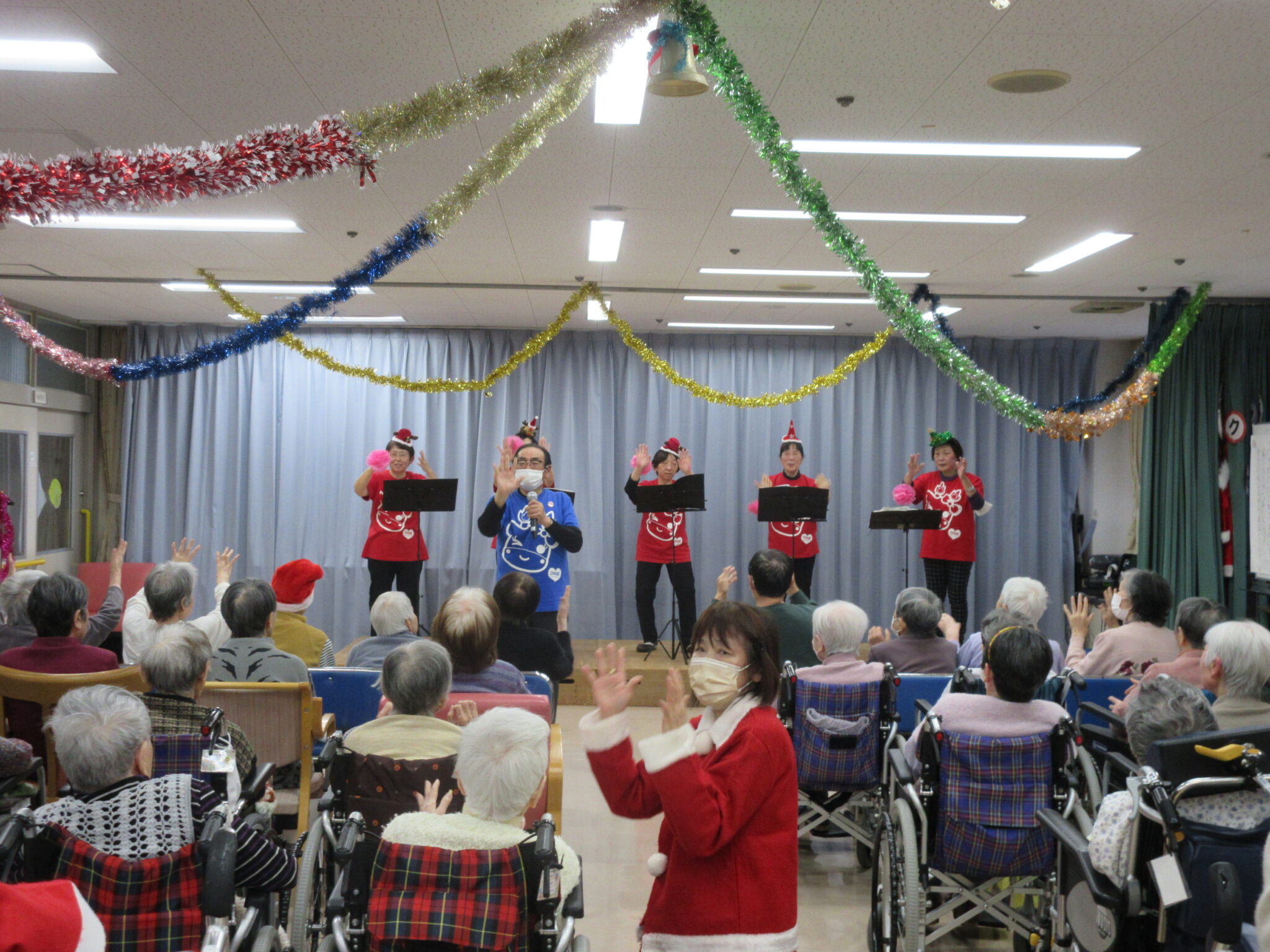 クリスマス時期の施設内イベント。入居者が舞台上のパフォーマンスを鑑賞している。